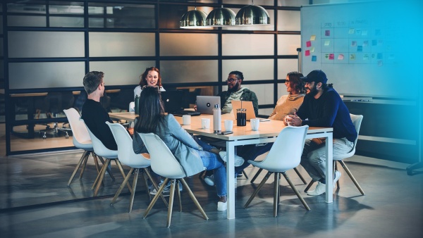 Six people are sitting in a meeting room at a table, appearing positive and engaged.